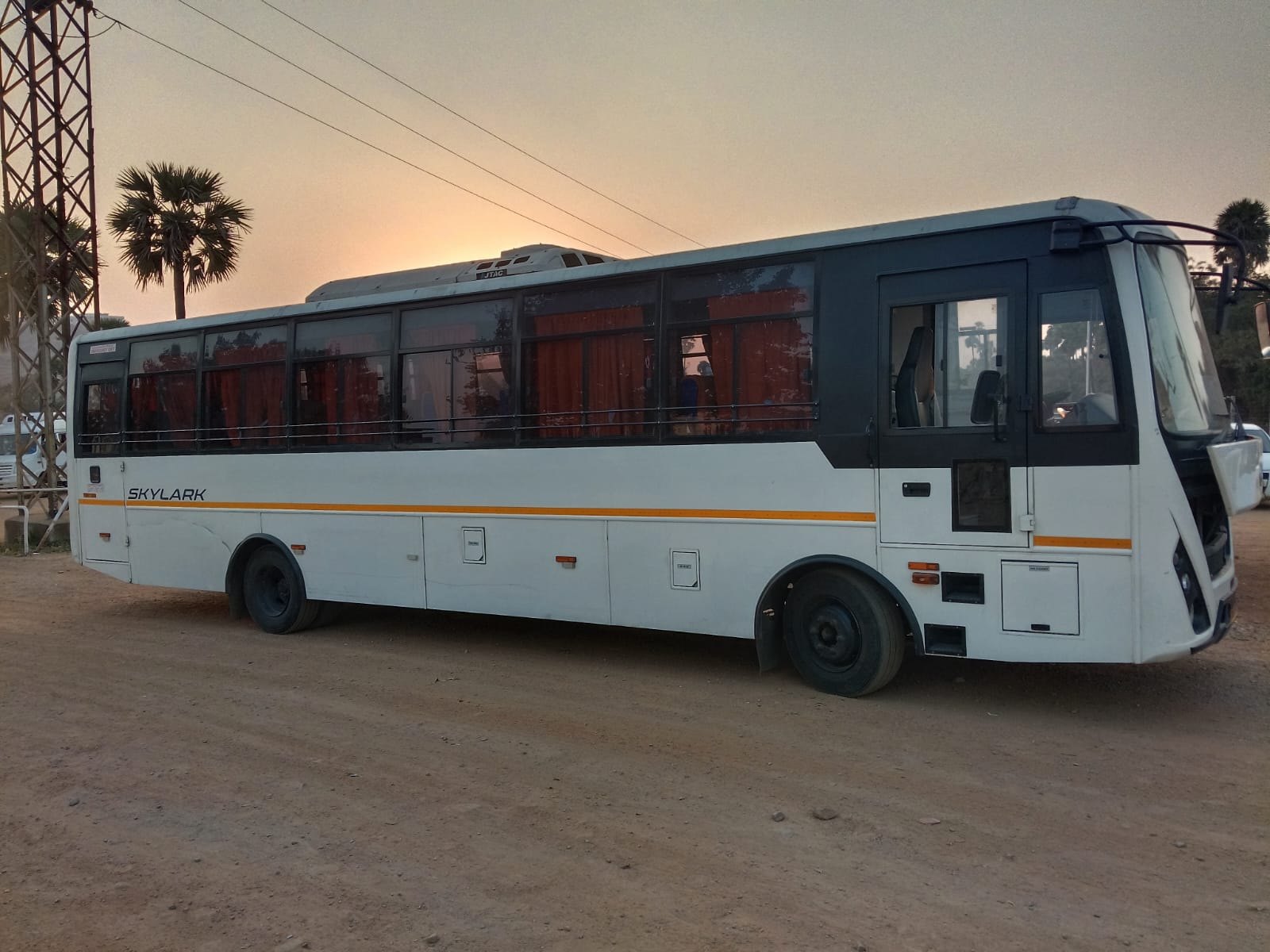 Full-size white JP Travels tourist coach parked at sunset