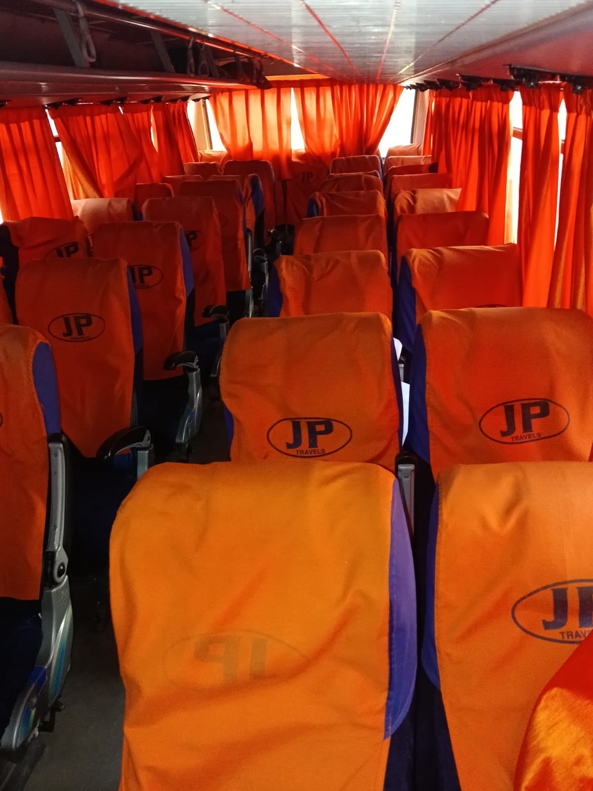 Interior of a JP Travels coach with orange seat covers carrying the JP Travels logo
