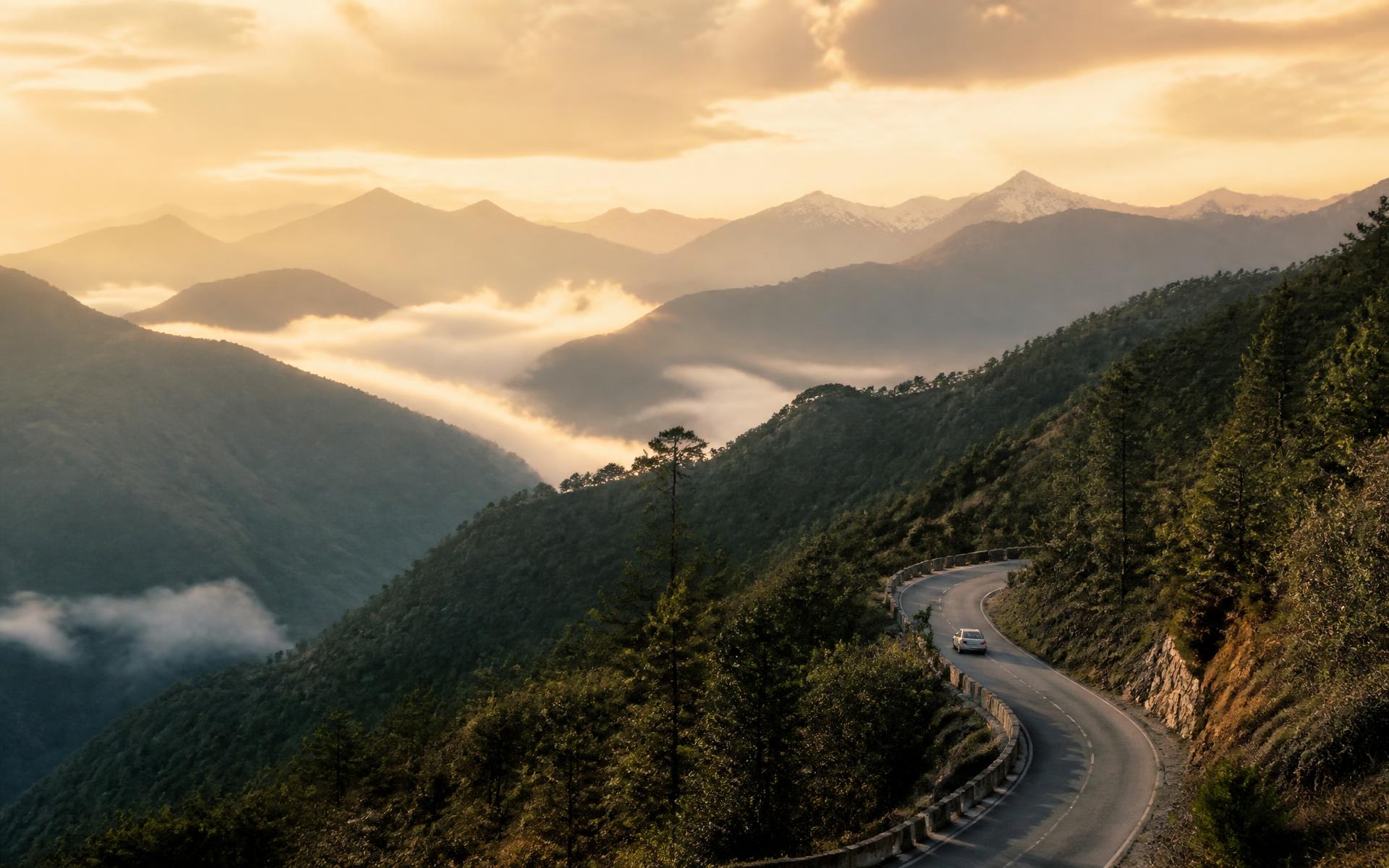 A car on a winding mountain road above mist-filled Himalayan valleys at golden hour